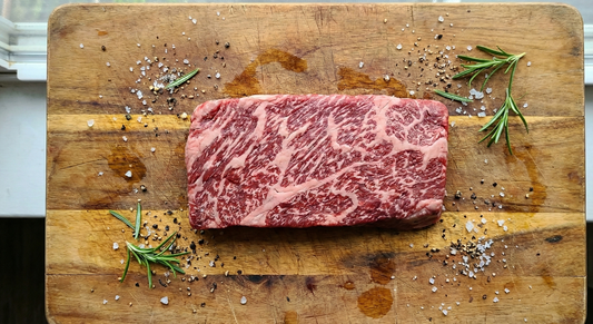 Raw marbled beef on a wooden cutting board with herbs and spices