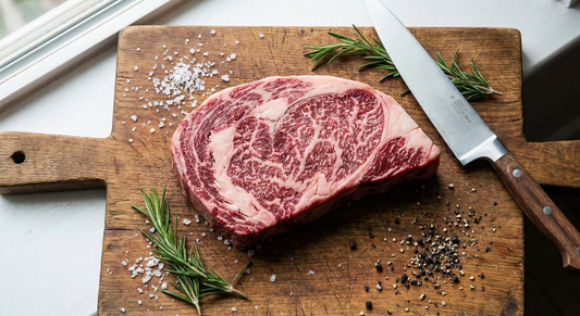 Raw American Wagyu Ribeye steak on a cutting board with salt and rosemary
